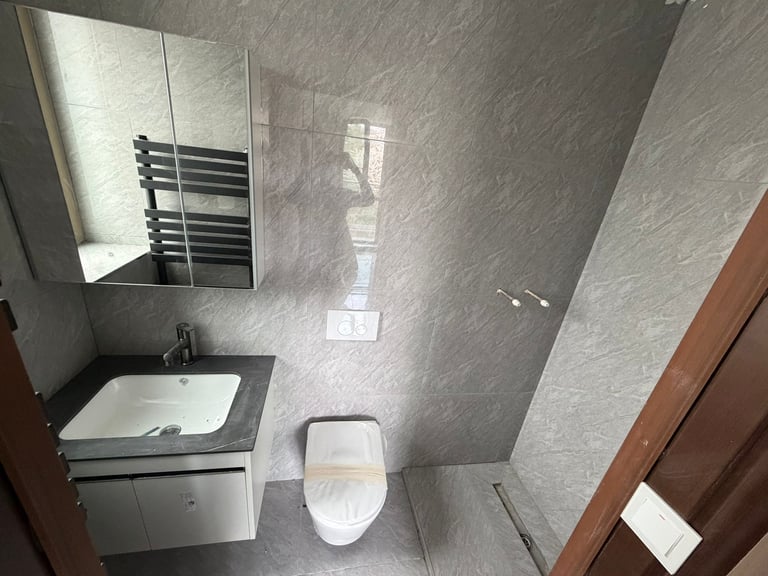 Modern bathroom interior with light gray tile walls, white toilet, sink with mirror cabinet, and shower area with glass partition