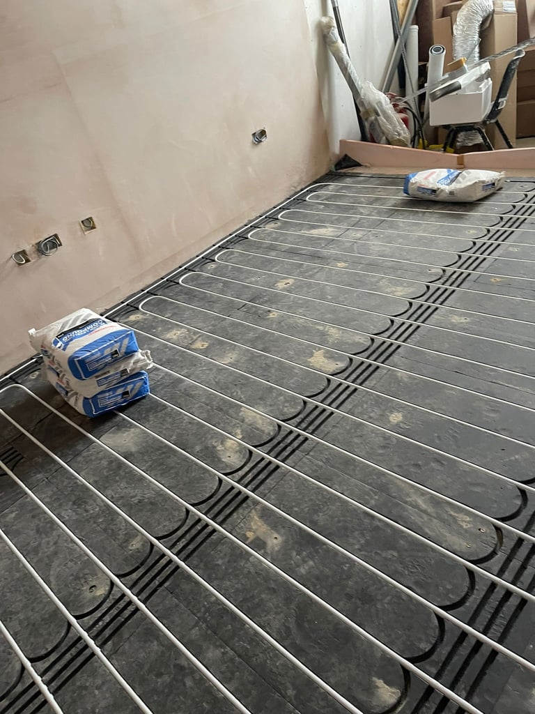 Radiant floor heating system with black tubing installed under concrete floor in construction space with unfinished drywall walls
