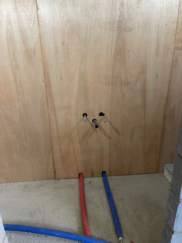 Unfinished wood wall with electrical outlet boxes and colored conduit pipes on concrete floor during construction