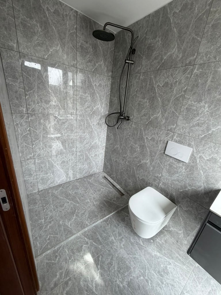 Modern bathroom with gray tile walls and floor, featuring a black rainfall showerhead, white toilet, and minimal fixtures in a compact space