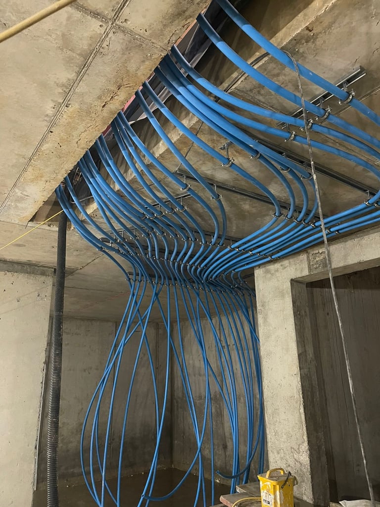 Multiple blue electrical cables and conduits running across a concrete ceiling in an unfinished building interior