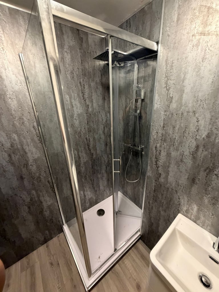 Modern corner shower enclosure with glass doors, overhead rainfall showerhead, and dark gray textured tile walls in a contemporary bathroom