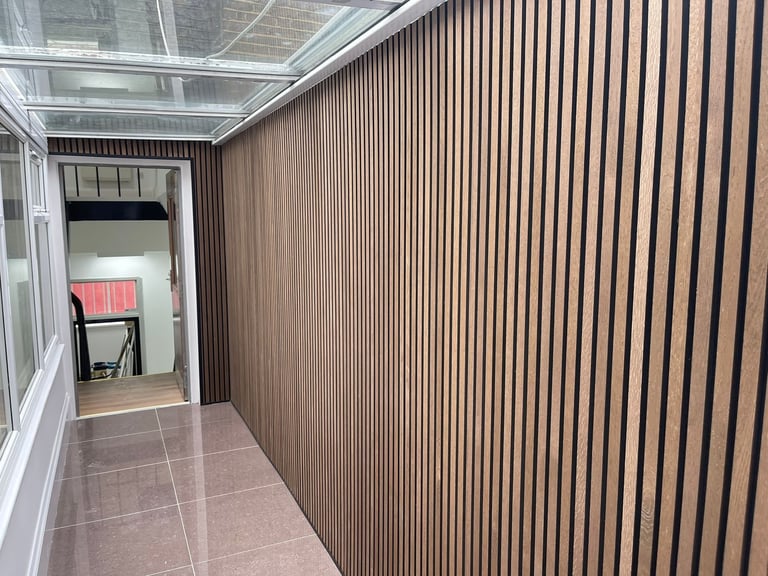 Modern narrow hallway with vertical wood paneling on right wall, tiled floor, and glass door entrance on left leading to interior space