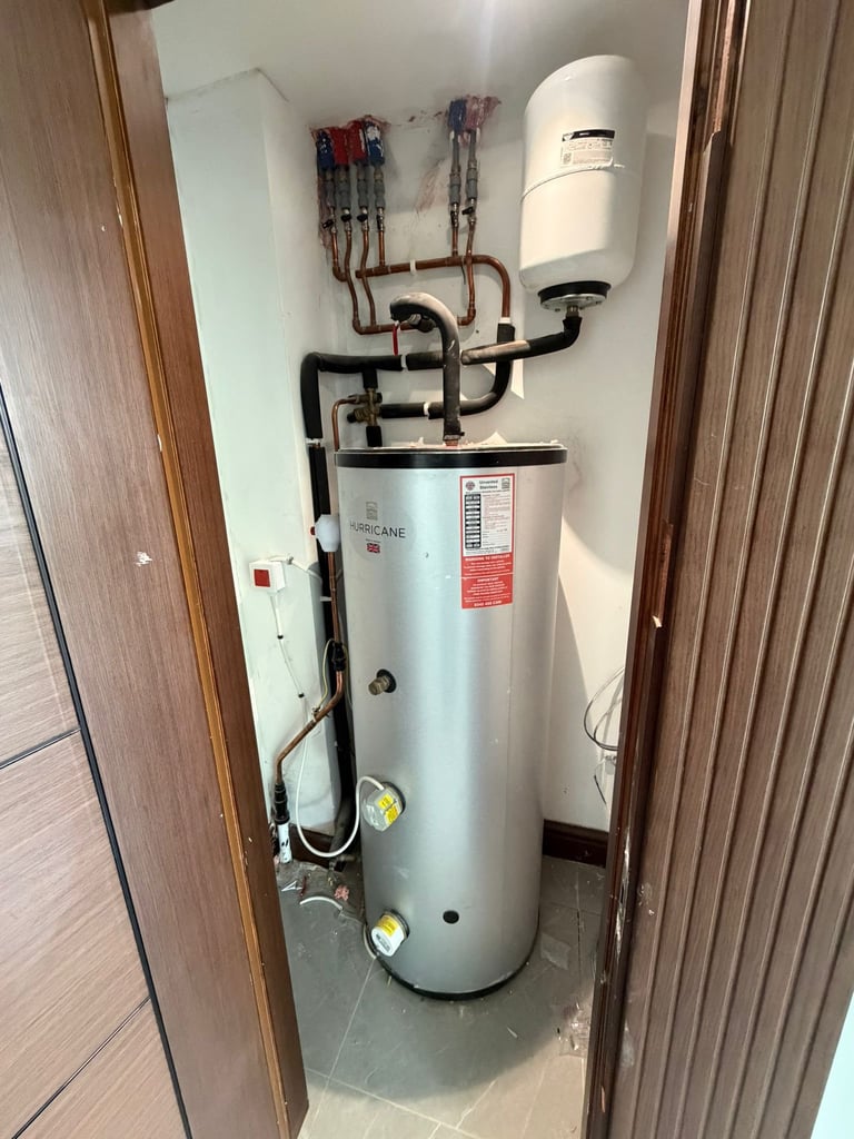 Water heater system with expansion tank mounted on wall in utility closet with copper and black piping connections