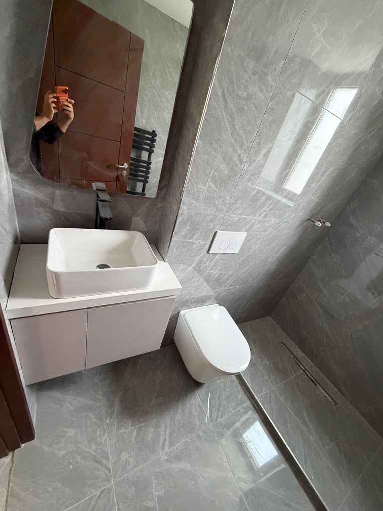 Modern bathroom with white vanity sink and toilet, gray tile walls, and mirror with brown frame