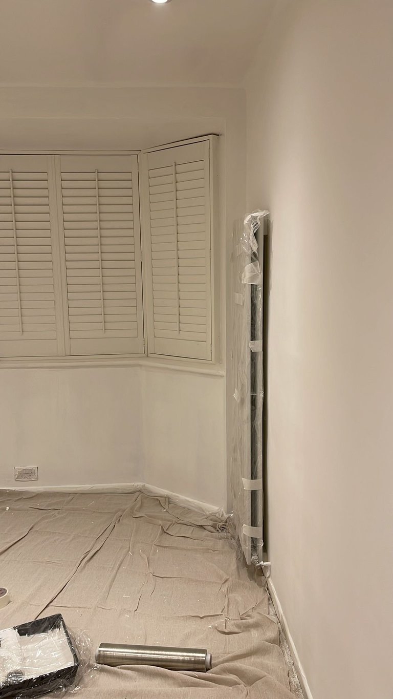 Interior room under construction with white louvered shutters on wall and plastic sheeting on floor with materials