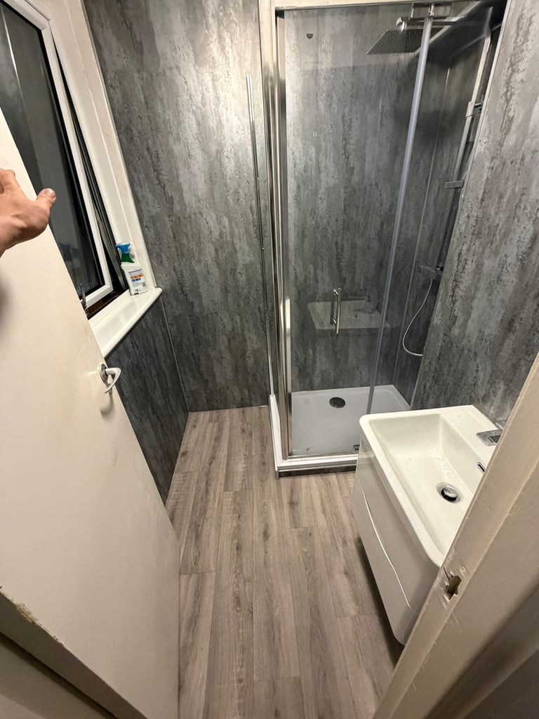 Modern bathroom with walk-in shower enclosure, white sink, wood-look tile flooring, and gray tile walls