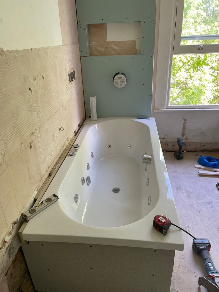 White whirlpool bathtub installed in a bathroom under renovation with drywall preparation and tools visible
