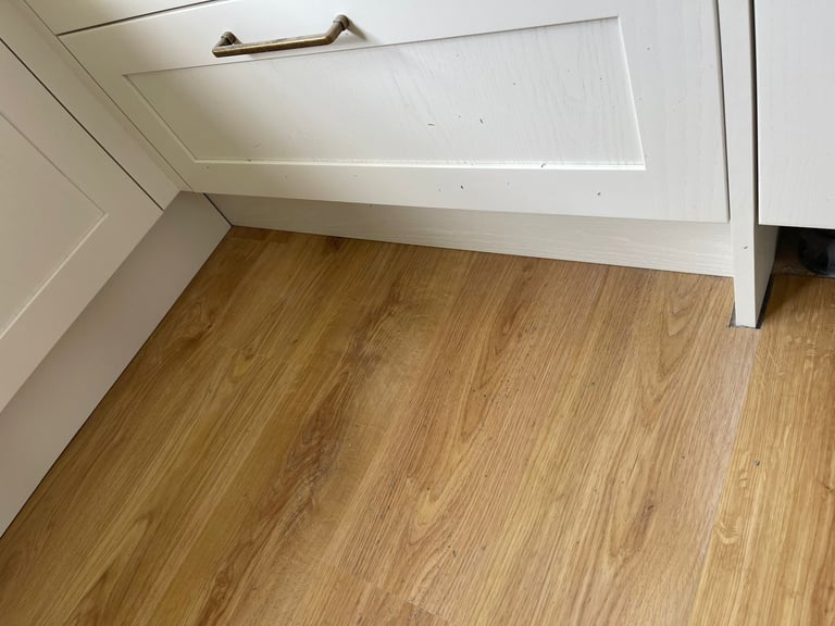 Wood laminate flooring next to white baseboards and cabinetry in a modern room interior